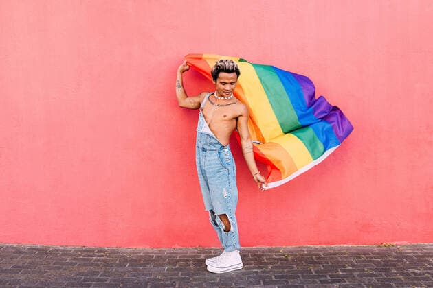 IMAGO Creative: Pride Month, Juni 2022 Gay male holding a rainbow LGBT flag in city against pink wall Copyright: xArtemxVarnitsinxArtemxVarnitsinx