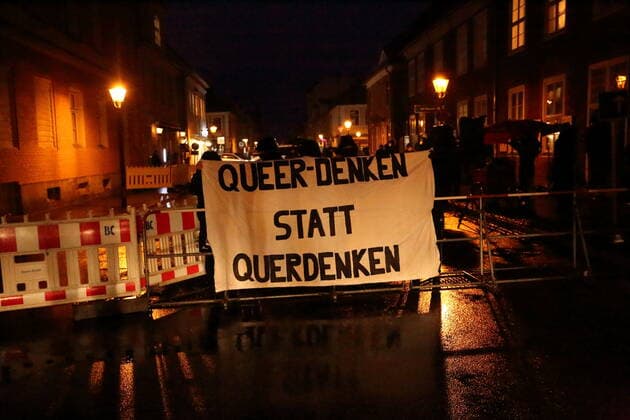 Gegendemonstranten stehen mit Banner Queer denken statt querdenken in der Gutenbergstraße während einer Demonstration gegen die Impfpflicht in der Coronavirus-Pandemie, Potsdam, 21. Februar 2022. Demo gegen Impfpflicht