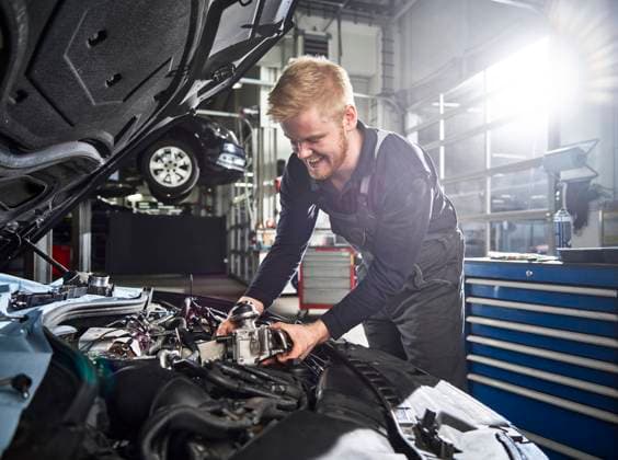 Smiling young blond mechanic repairing car engine in auto shop model released property released, CVF01880
