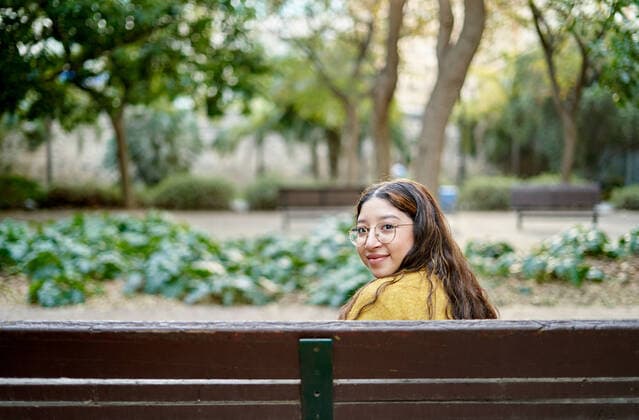 Creative Highlights Symbolbilder Optimistic young female looking at camera through shoulder while sitting on wooden bench in park with green plants on summer day AdalbertoRodriguez_WomanWithDog_35.jpg Copyright: xAdalbertoxRodriguezx Model Released