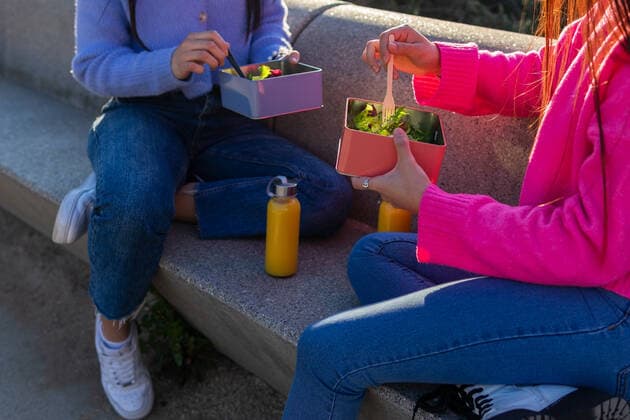 IMAGO Creative, Jahreszeit Sommer, Sommer in der Stadt Side view of anonymous cheerful Hispanic female friends eating salad while sitting on stone bench with water bottles on sunny street DavidMunoz_JenniferAndAlejandraLifestyle_2.jpg Copyright: xDavidxMunozx Model Released
