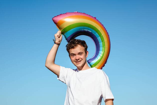Creative Highlights Symbolbilder Joyful transgender male with rainbow shaped balloon with LGBT symbol in raised hands standing on blue background on sunny day HodeiUnzueta_TransgenderManInTheBeach_18.jpg Copyright: xHodeixUnzuetax Model Released