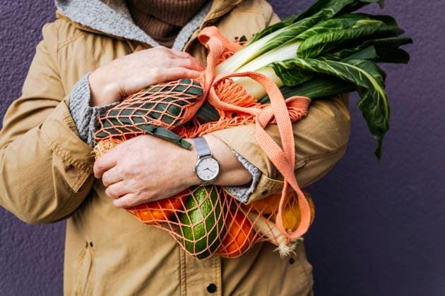 Woman holding mesh bag with vegetables in front of purple wall model released, IHF00750