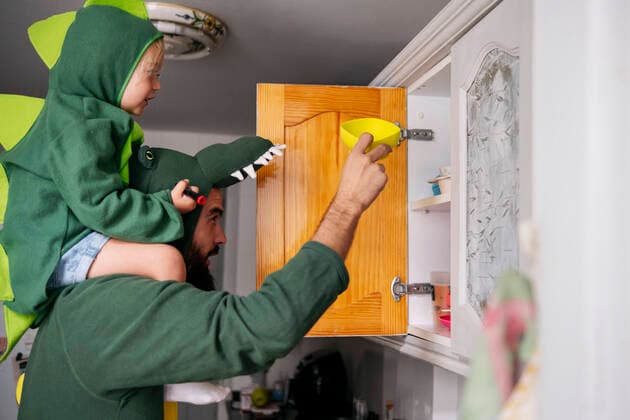 IMAGO Creative: Vaterschaft Father and son in dinosaur costumes removing bowl from cabinet at home model released property released, ASGF02135