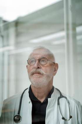 IMAGO Creative: Lokalhelden - Gesundheits- und Rettungskräfte Thoughtful doctor with mustache wearing eyeglasses at medical clinic model released property released, JOSEF07350