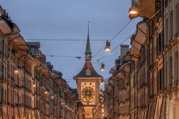 Switzerland, Canton of Bern, Bern, Street lights and power lines stretching over old town street at dusk with Zytglogge clock tower in background, KEBF02254