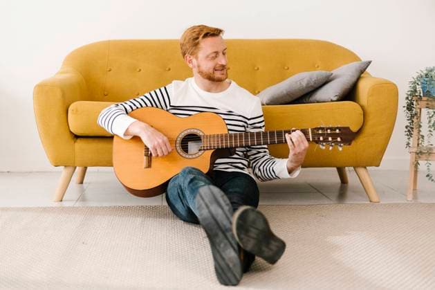 Young man playing guitar sitting in front of sofa at home model released property released, XLGF02886
