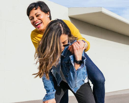 IMAGO Creative: Urban Diversity Creative Highlights Symbolbilder Woman giving piggyback ride to cheerful black female friend while having fun together on sunny street near building in city, Model released DavidMunoz_FriedsHostel_13.jpg Copyright: xDavidxMunozx MR
