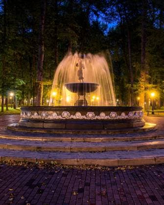 A fountain with blurred streams of water in a night park illuminated by lanterns with a stone pavement, trees and benches. Cityscape., model released, , property released, , 33686914.jpg, fountain, flow, splash, night, darkness, stream, wet, light, urban, decorative, scene, drop, liquid, spray, luminous, evening, city, park, illumination, ripple, water, geometric, lantern, dusk, square, nighttime, pavement, twilight, autumn, outdoor, bright, architecture, cityscape, europe, bench, nocturnal, fall, summer, tourism, trunk, maple, townscape, lawn, grass, alley, scenic, place, road, town, leaf,