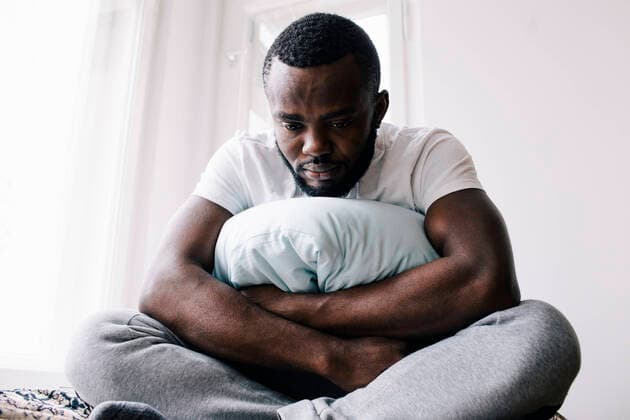 Emotionally stressed man sitting cross-legged with pillow in bedroom at home Germany, Berlin, model released, property released Copyright: xMaskotx , MA92684