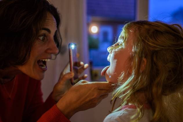 Eine Frau schaut einem Kind in den Rachen. Als Lampe dient ein Smartphone, Das Kind streckt die Zunge heraus. *** A woman looks into the throat of a child A smartphone serves as a lamp, The child sticks out his tongue