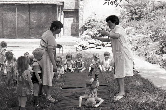 21.07.1988, Magdeburg, Bezirk Magdeburg, DDR - Kinder in einem Kindergarten machen Sport. (80er Jahre, abrollen, Achtziger Jahre, aktiv, Aktivitaet, Alltag, aussen, Aussenaufnahme, bewegen, Bewegung, Bezirk Magdeburg, bis 10 Jahre, DDR, deutsch, Deutsche Demokratische Republik, Deutschland, Europa, europaeisch, Fitness, Frauen, GDR, gemeinsam, Gesellschaft, Gruppe, Historie, historisch, im Freien, Jahreszeit, Kaukasier, kaukasisch, Kinder, Kinderbetreuung, Kindergaertnerin, Kindergaertnerinnen, Kindergarten, Kindergartenalltag, Kindergartenkinder, Kindergartenplatz, Kindertagesbetreuung, Kindertagesstaette, Kinderturnen, Kindheit, Kita, Kleinkinder, Leibeserziehung, Leibesuebung, Magdeburg, Matte, Menschen, Personen, pmscartandhistory, Purz
