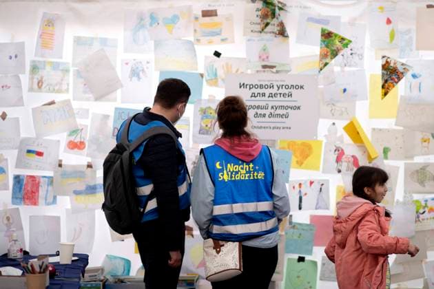 Ukraine, Refugees DEU, Deutschland, Germany, Berlin, 22.03.2022 Freiwillige Helfer Nachtsolidaritaet vor einer Wand mit Zeichnungen von Kindern in der Children™s Play area im Ankunftszentrum. Ankunft von Fluechtlingen aus der Ukraine am Hauptbahnhof Berlin, Deutschland. Die Fluechtlinge zumeist Frauen und Kinder fliehen vor dem Krieg in der Ukraine nach der Invasion von Russland und erhalten Unterstuetzung von Freiwilligen. Zehntausende Flüchtlinge, die nach der russischen Militaerinvasion vor dem anhaltenden Krieg in der Ukraine geflohen sind, sind in den letzten Wochen hauptsaechlich mit Zuegen ueber Polen angekommen. en: Night Solidarity Volunteers in front of a wall with children s drawings in the Children s Play area in the Arrivals
