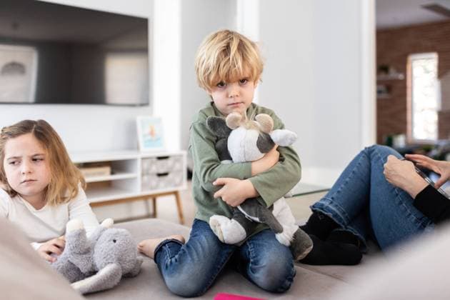 Unhappy boy with toy looking at camera while sitting on sofa near sad sister in light living room at home, Model released, Property released AngelSantamaria_DigitalDependency_11.jpg Copyright: xAngelxSantamariax MR