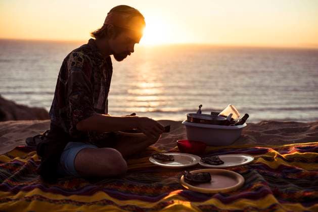 IMAGO Creative: Ende des Sommers Sunset glow over ocean as man makes picnic dinner in sand Portugal Melides, Setubal, Portugal CR_PIDODS220414-672631-01 ,model released, Symbolfoto