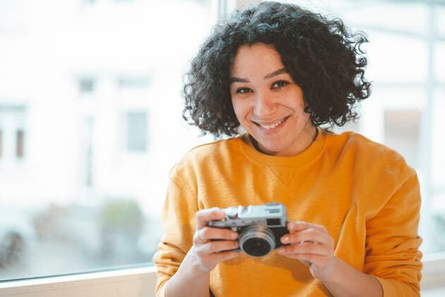 Smiling woman with camera sitting by window at home model released, Symbolfoto property released, JOSEF07849
