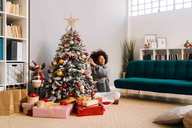 Smiling young woman sitting cross-legged decorating Christmas tree at home in living room model released, Symbolfoto property released, GIOF15282