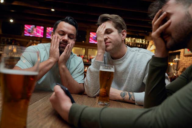 Three frustrated male soccer fans having beer and watching a match on smartphone in a pub model released, Symbolfoto property released, ABIF01693