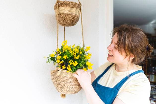 Smiling woman planting in basket hanging in front of wall model released, Symbolfoto property released, IHF00778