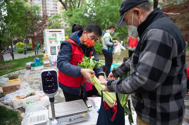 (220428) -- BEIJING, April 28, 2022 -- A supermarket employee (L) helps a resident pack vegetables at a temporary stand selling daily necessities in a community in Chaoyang District of Beijing, capital of China, April 28, 2022. During the latest resurgence of COVID-19 infections in Beijing, people from different walks of life have joined the fight against the coronavirus, working against the clock to offer hearty support. ) CHINA-BEIJING-COVID-19 (CN) ChenxZhonghao 