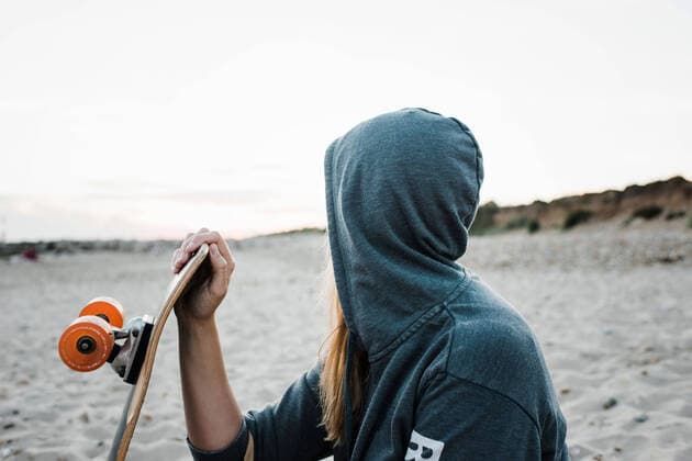 IMAGO Creative: Sommer Sport - Strand woman with her hood up at the beach holding skateboard at sunset Christchurch, England, United Kingdom CR_RABE210920-830236-01 ,model released, Symbolfoto