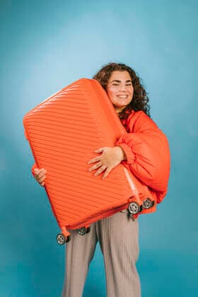 Creative Highlights Symbolbilder Happy young woman carrying orange suitcase against blue background model released, Symbolfoto, MMPF00002