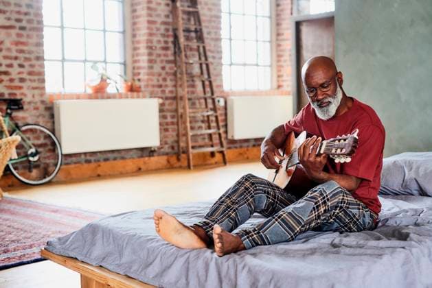 Man with eyeglasses playing guitar on bed at home model released, Symbolfoto property released, FMKF07456
