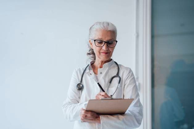 IMAGO Creative: Lokalhelden - Gesundheits- und Rettungskräfte Senior doctor writing on clipboard model released, Symbolfoto property released, JOSEF08975