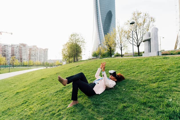 IMAGO Creative: Internationaler Tag der Architektur am 3. Oktober. Thema: Architektur zum Wohlfühlen Businesswoman wearing virtual reality simulator lying on grass gesturing in city model released, Symbolfoto, MEUF05463