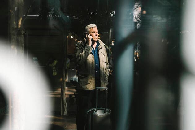 IMAGO Creative: Welttourismustag am 27. September Businessman talking on smart phone while standing by wheeled luggage at railroad Station Sweden, Gothenburg, model released Copyright: xMaskotx , MA94026