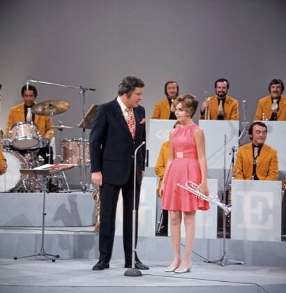 DREI MAL NEUN Drei mal Neun, ZDF Quizshow, Deutschland, 1971, im Bild: Showmaster Wim Thoelke im Gespräch mit der amerikanischen Trompetensolistin Carole Dawn Reinhart, im Hintergrund: Musiker der Max Greger Bigband. Drei mal Neun, TV quiz show, Germany, 1971, on the photo: presenter Wim Thoelke talks with American trumpet soloist Carole Dawn Reinhart, in the background: musicians from the Max Greger Big Band., Deutschland Copyright: ArthurxGrimm UnitedArchives82007898 EDITORIAL USE ONLY