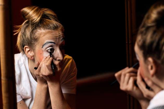 Young professional female mime in casual clothes painting the eyes and looking in mirror in dressing room JavierBallester_PippiClown_00006.jpg Copyright: xJavierxBallesterx Model Released