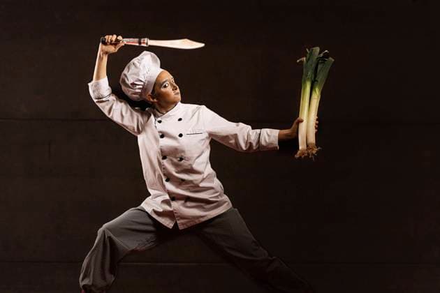 Funny young female clown in chef costume with makeup doing martial arts pose before cutting fresh leeks with knife on stage JavierBallester_PippiClown_00021.jpg Copyright: xJavierxBallesterx Model Released