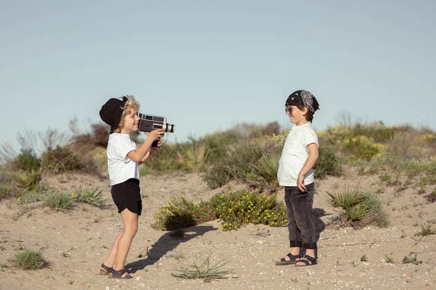 IMAGO Kreativ: Bruderschaft Full body side view of stylish little boy in casual clothes taking video of cheerful brother while standing together on sandy beach under blue sky on sunny summer day SinuheGorris_EveningWithFriends_00007.jpg Copyright: xSinuhexGorrisx Model Released