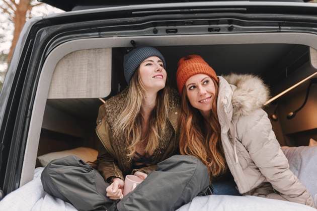 IMAGO Creative: Herbst, Touren mit dem Camper Smiling women with long hair wearing knit hats sitting in motor home model released, Symbolfoto, MRRF02104