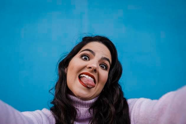 Creative Highlights Symbolbilder Playful of happy woman sticking out tongue taking selfie in front of blue wall model released, Symbolfoto, DCRF01211