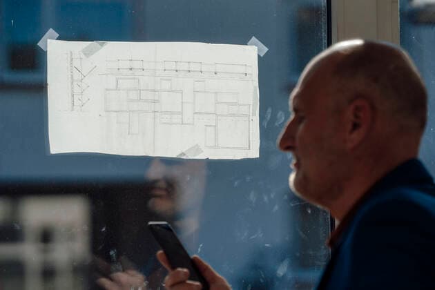 Businessman with mobile phone by blueprint on window in office model released, Symbolfoto property released, JOSEF09777