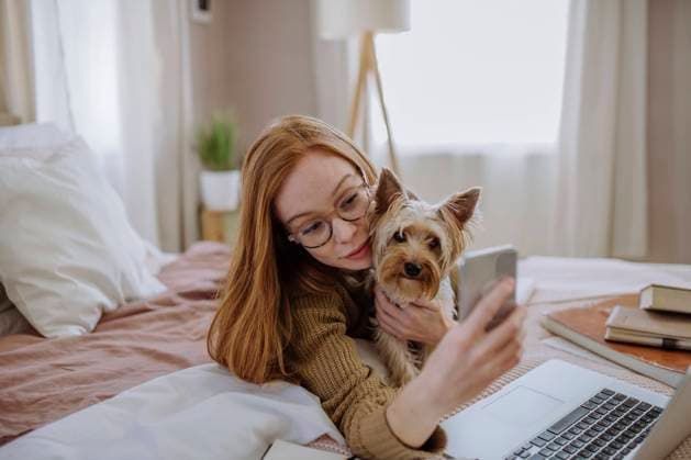 Smiling woman taking selfie with pet dog through smart phone lying on bed at home model released, Symbolfoto property released, HAPF03132