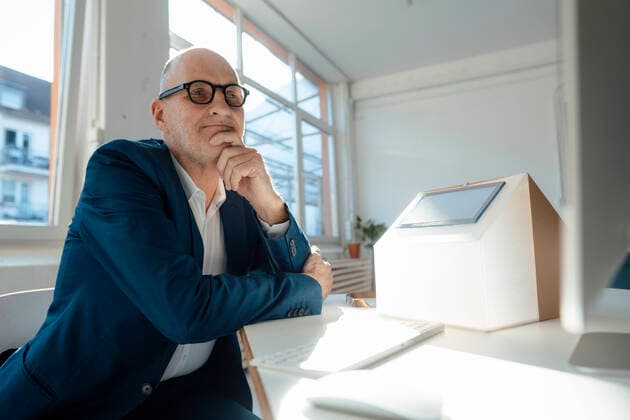 IMAGO Creative: Internationaler Tag der Architektur am 3. Oktober. Thema: Architektur zum Wohlfühlen Thoughtful businessman with house model looking at computer in office model released, Symbolfoto property released, JOSEF09864