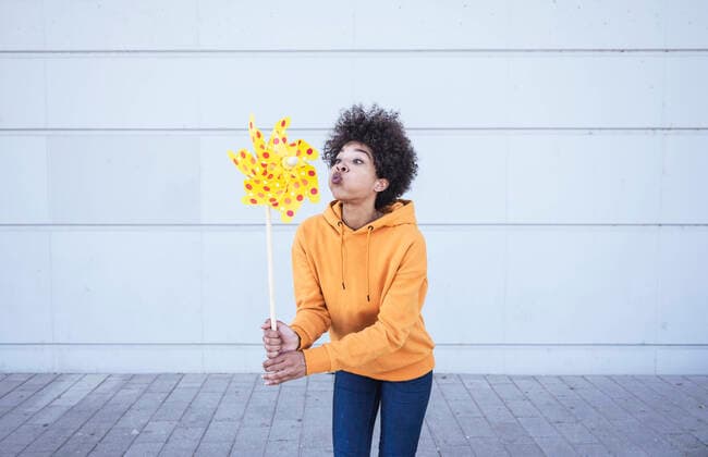 Creative Highlights Symbolbilder Woman playing with yellow pinwheel standing in front of wall model released, Symbolfoto, UUF26207