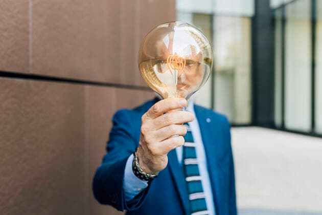 Creative Highlights Symbolbilder Senior businessman holding light bulb standing by wall model released, Symbolfoto, MEUF06251
