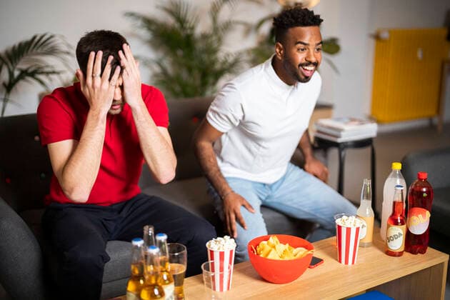 Happy man watching football match by sad roommate at home model released, Symbolfoto property released, Florence Florence Italy SBAF00115