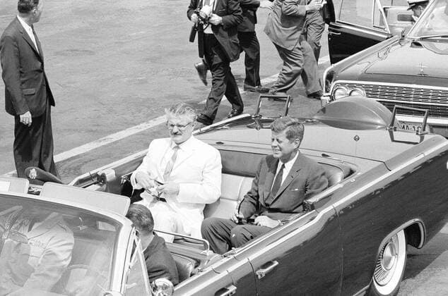 Arrival ceremony for Carlos Julio Arosemena Monroy, President of Ecuador, 11:00AM. President John F. Kennedy and President of the Republic of Ecuador, Dr. Carlos Julio Arosemena Monroy, sit in the back seat of the presidential limousine (Lincoln-Mercury Continental convertible), following the arrival ceremony in honor of President Arosemena Monroy. Seated in front seat: Military Aide to President Kennedy, General Chester V. Clifton (passenger seat), and White House Secret Service agent, Bill Greer (drivers seat). Naval Aide to President Kennedy, Captain Tazewell T. Shepard, Jr. (far right, partially hidden), steps out of car in background; Secret Service agent, Emory Roberts, stands at left. Military Air Transport Service (MATS) terminal, W Copyright: xpiemagsx