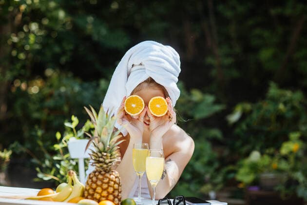 Creative Highlights Symbolbilder Woman wrapped in white towels covering eyes with halves of orange while sitting at table with fresh fruits on patio, Model released CamilleGirard_WomanOnPatio_00027.jpg Copyright: xCamillexGirardx MR