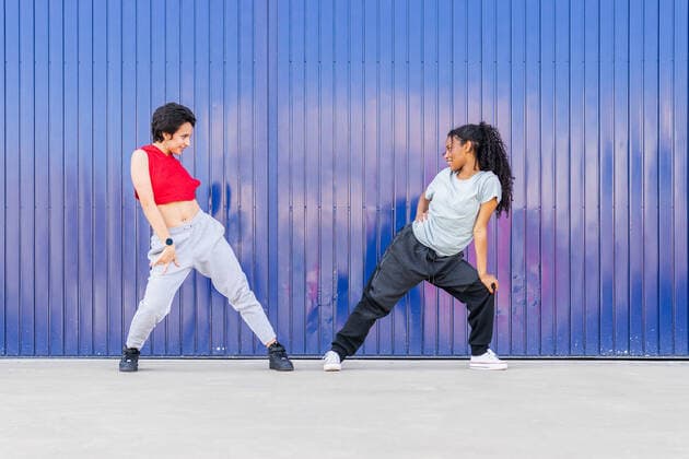 Full body side view of multiracial young female friends dancing on street near blue wall in city DavidMunoz_CarlaAndNicoleFiraDance_35.jpg Copyright: xDavidxMunozx Model Released