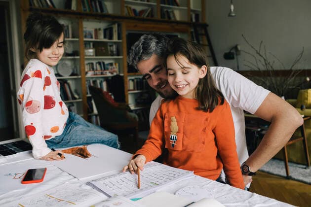 IMAGO Creative: Vaterschaft Smiling father looking at daughter reading book while girl sitting on table Berlin, Germany, model released, property released Copyright: xMaskotx , MA93040 MA93040