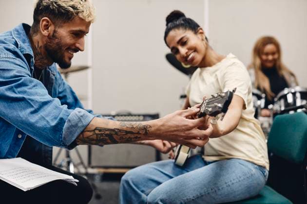 Smiling young man teaching woman guitar while rehearsing in classroom Sweden, Stockholm, model released, property released Copyright: xMaskotx , MA93104 MA93104