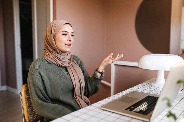 Female freelancer in hijab gesturing during video call through laptop while working at home Sweden, Gothenburg, model released, property released Copyright: xMaskotx , MA93274 MA93274
