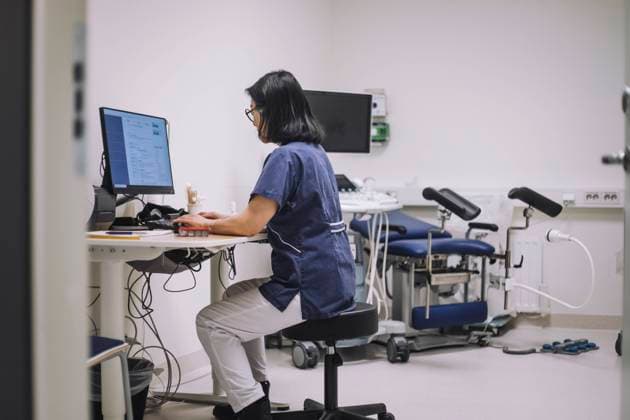 IMAGO Creative: Lokalhelden - Gesundheits- und Rettungskräfte Side view of female doctor using desktop PC sitting at desk in medical clinic Sweden, Stockholm, model released, property released Copyright: xMaskotx , MA94521 MA94521