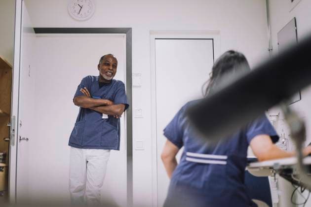 Smiling male doctor standing with arms crossed while talking with female colleague in medical clinic Sweden, Stockholm, model released, property released Copyright: xMaskotx , MA94527 MA94527